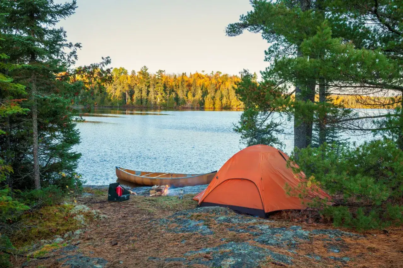 Idealny pomysł na weekend: namiot, canoe i ognisko nad jeziorem. Jesienne kolory drzew tworzą piękne tło.