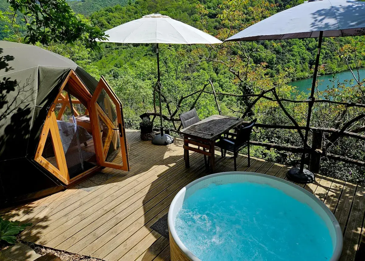 Domek w Gorges du Tarn z jacuzzi i widokiem na rzekę. Drewniany taras, stół z krzesłami i parasole.