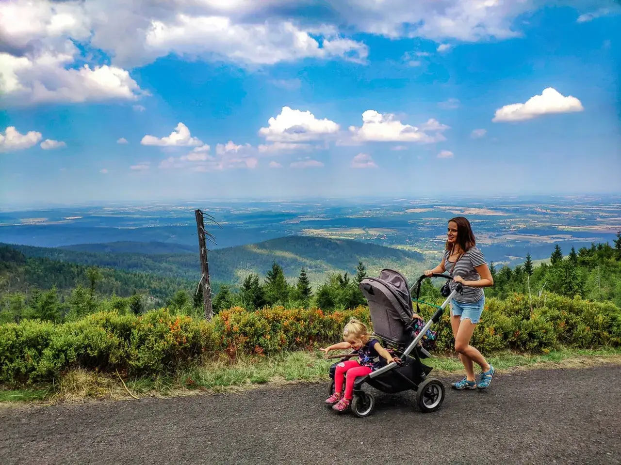 Mama z córką na spacerze, gdzie w góry z wózkiem. Widok na dolinę i chmury.