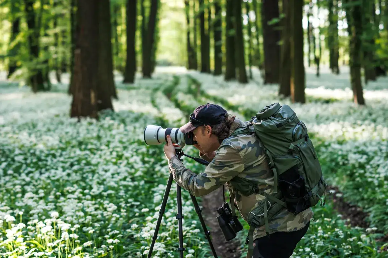 Fotograf w lesie, otoczony białymi kwiatami, ćwiczy swoje umiejętności w szkole fotografii.