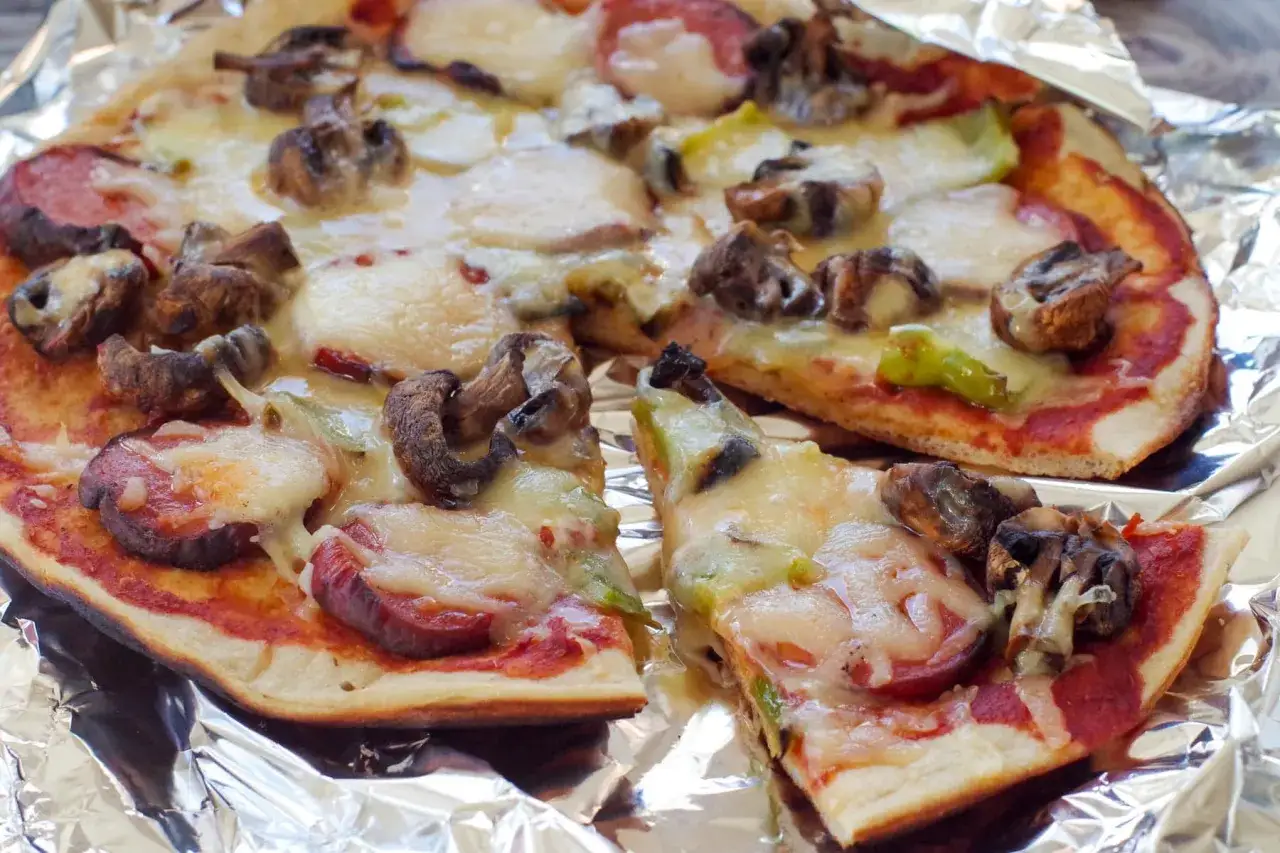 Pyszna pizza z grilla z pieczarkami i kiełbasą, roztopiony ser ciągnie się apetycznie.