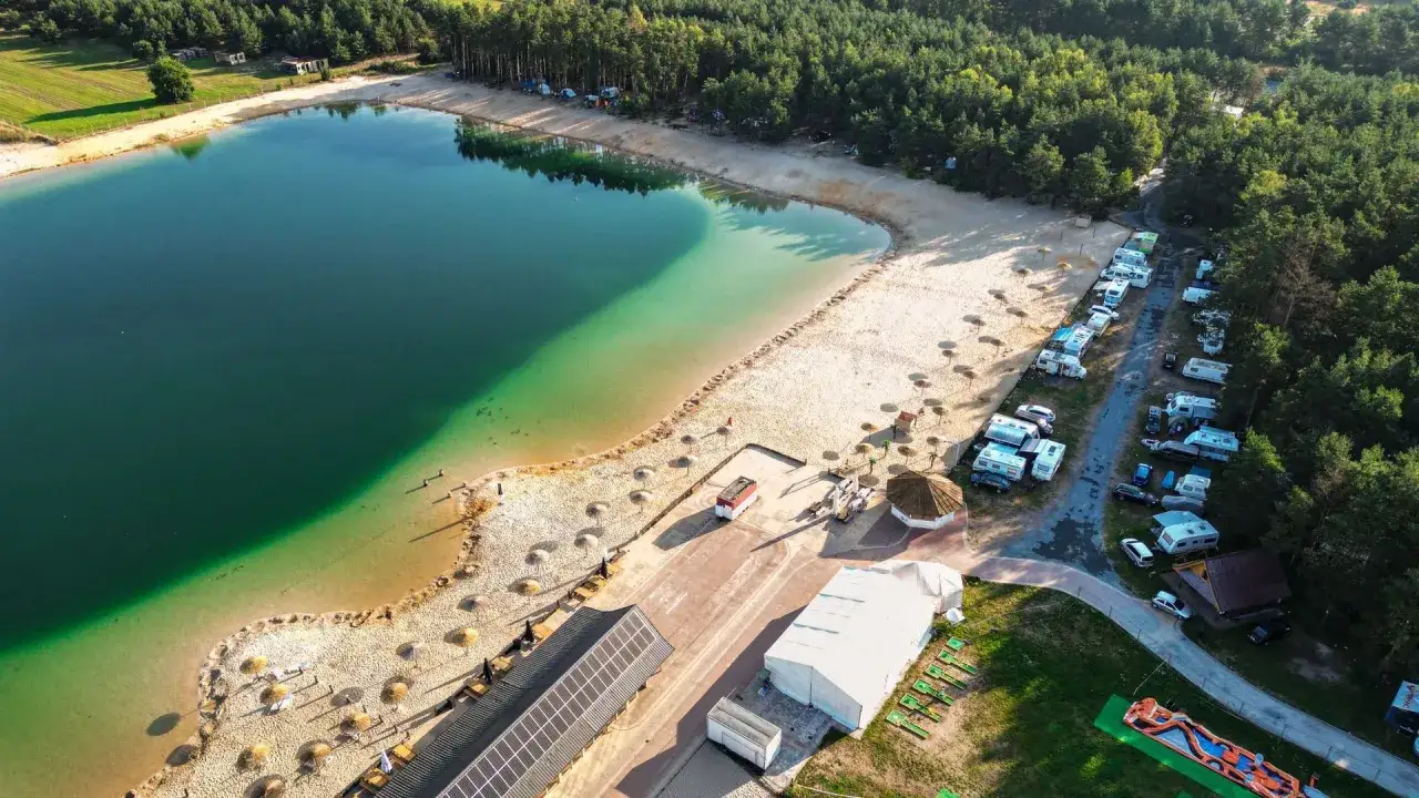 Idealne miejsce, gdzie na majówkę w Polsce: kemping z kamperami nad turkusowym jeziorem i piaszczystą plażą, otoczony lasem.