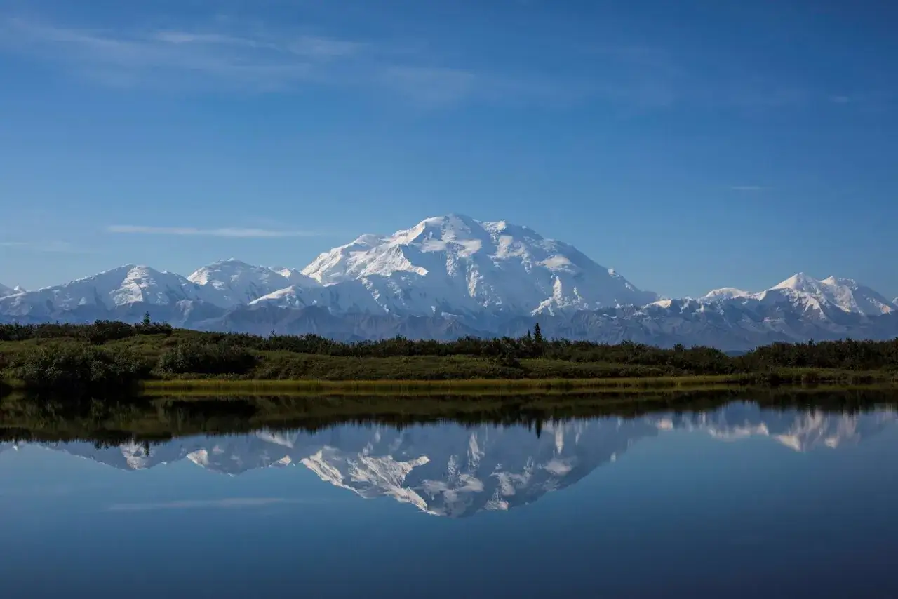 Majestatyczny, ośnieżony najwyższy szczyt Ameryki Północnej, Denali, odbija się w spokojnej tafli jeziora.