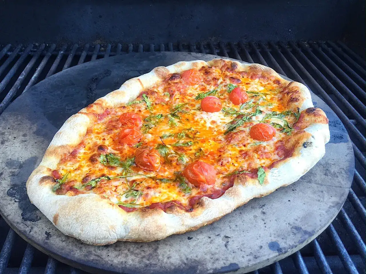 Pyszna pizza z grilla gazowego, z pomidorkami koktajlowymi i rukolą, na kamieniu.
