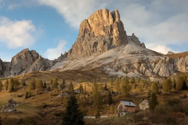 Jesienne słońce oświetla majestatyczne szczyty Dolomitów, idealne miejsce na trekking. Drewniana chata i drzewa tworzą malowniczy krajobraz.