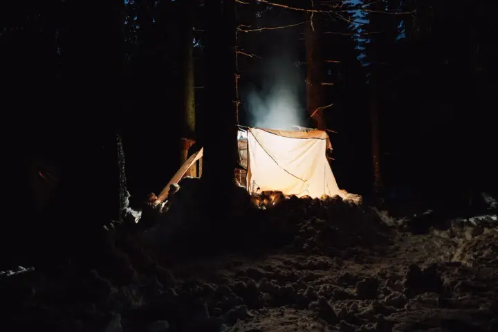 Nocne schronienie w lesie. Jasny namiot oświetla śnieżny krajobraz, tworząc przytulną atmosferę. Idealne miejsce, by zanocuj w lesie.