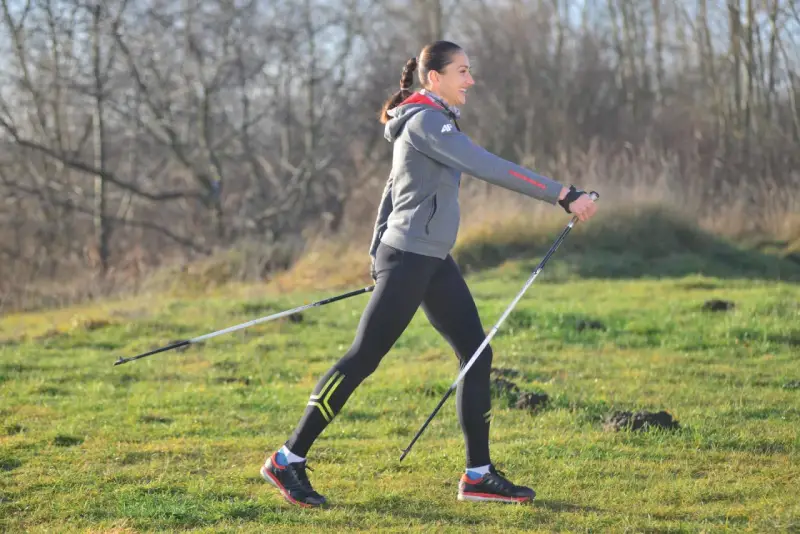 Kobieta w stroju sportowym ćwiczy nordic walking, używając kijków. Widać, jakie kije do nordic walking są lekkie i wygodne.